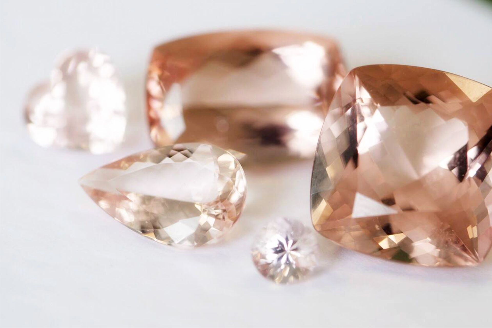 A collection of varied cuts of Morganite stones on a flat surface.