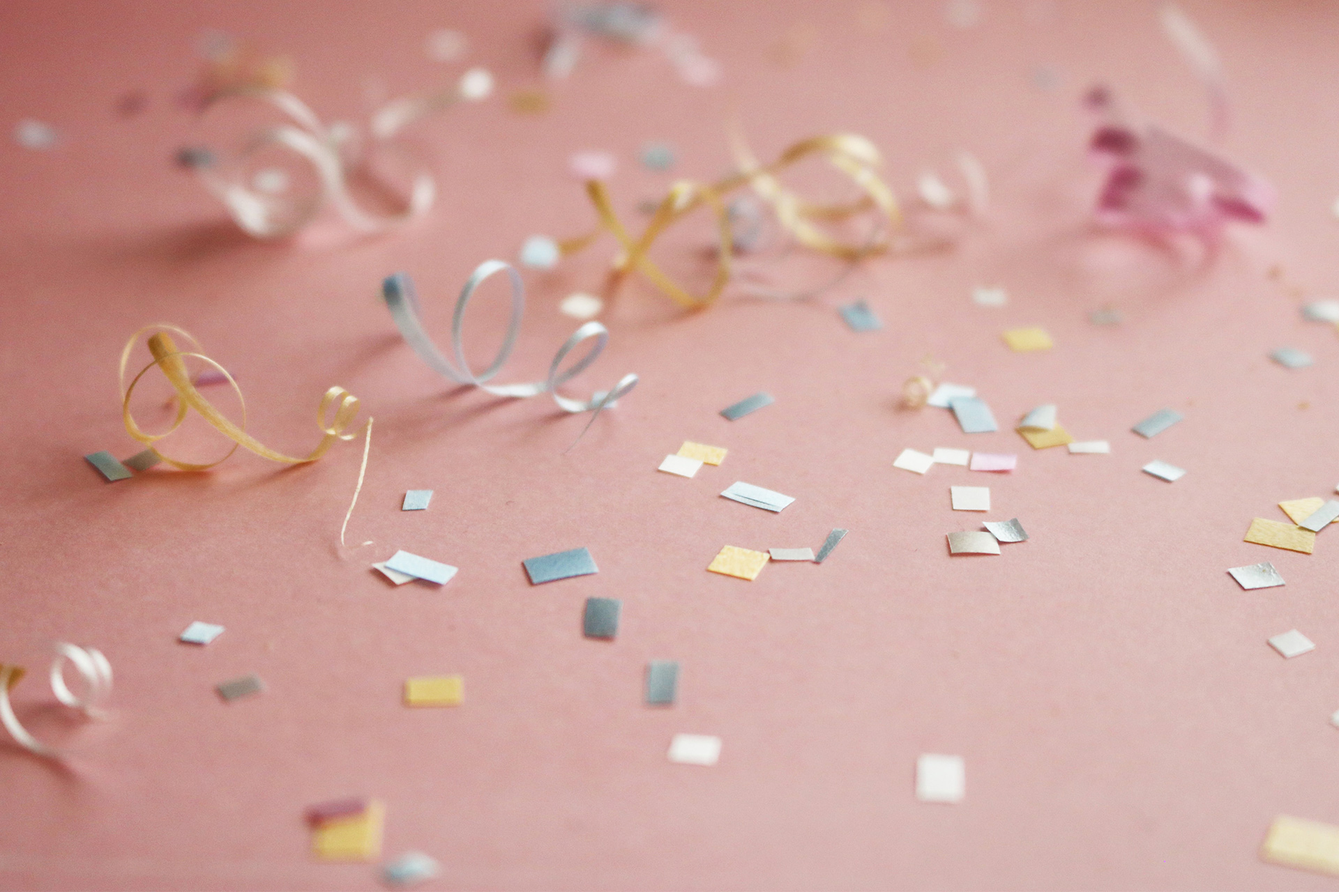 Pink surface covered with confetti in all shapes, colours and sizes.