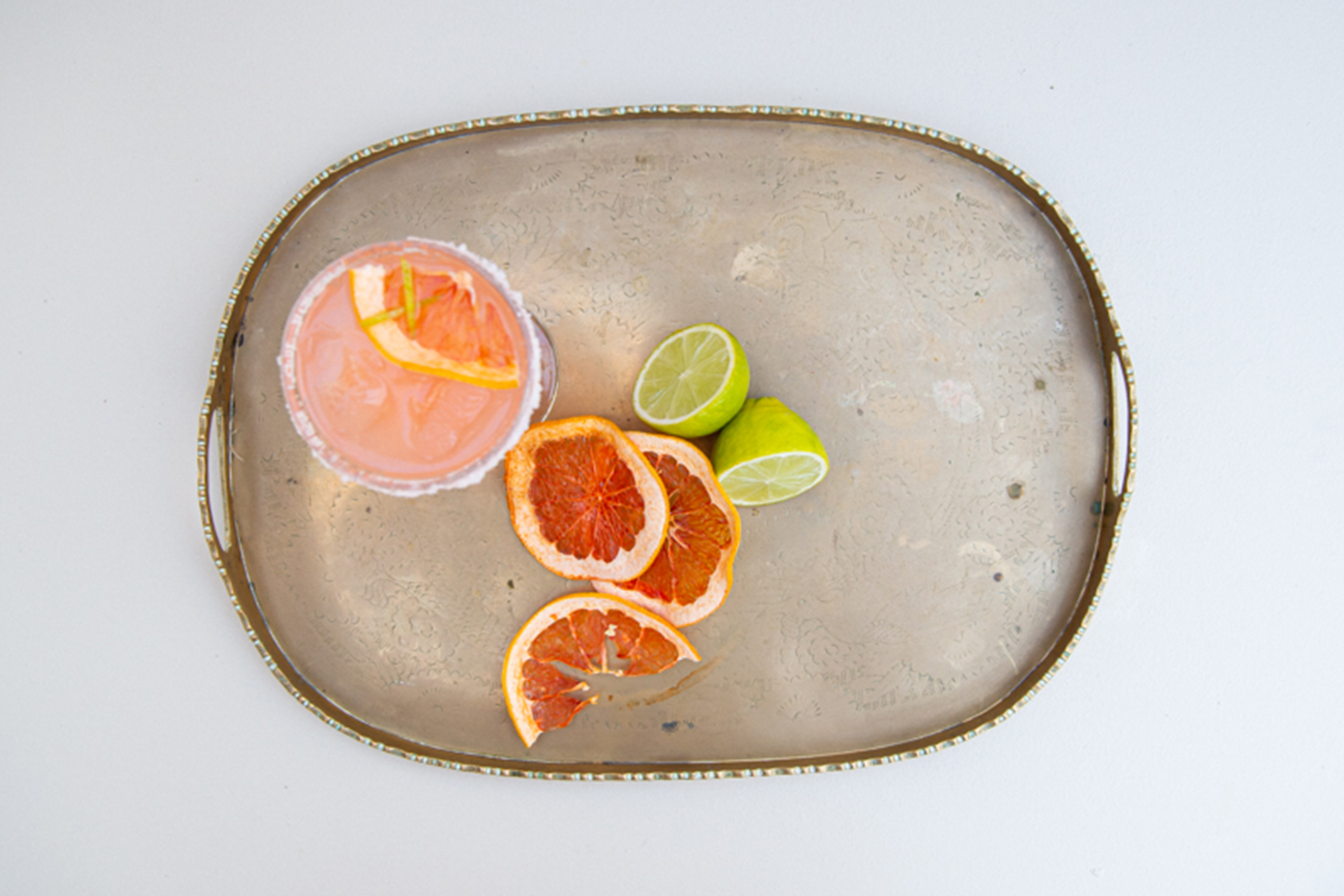 Tray with cocktail, slices of blood orange and a lemon cut in half