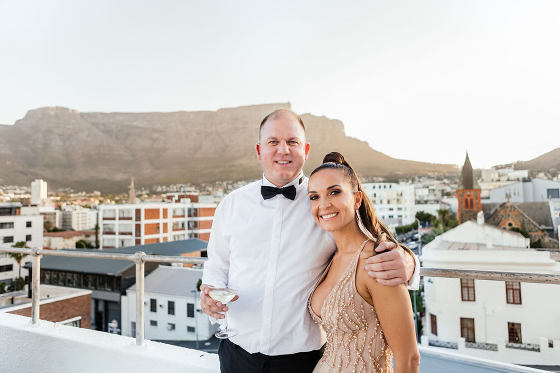 Husband and wife standing on a rooftop with cityscape in the background